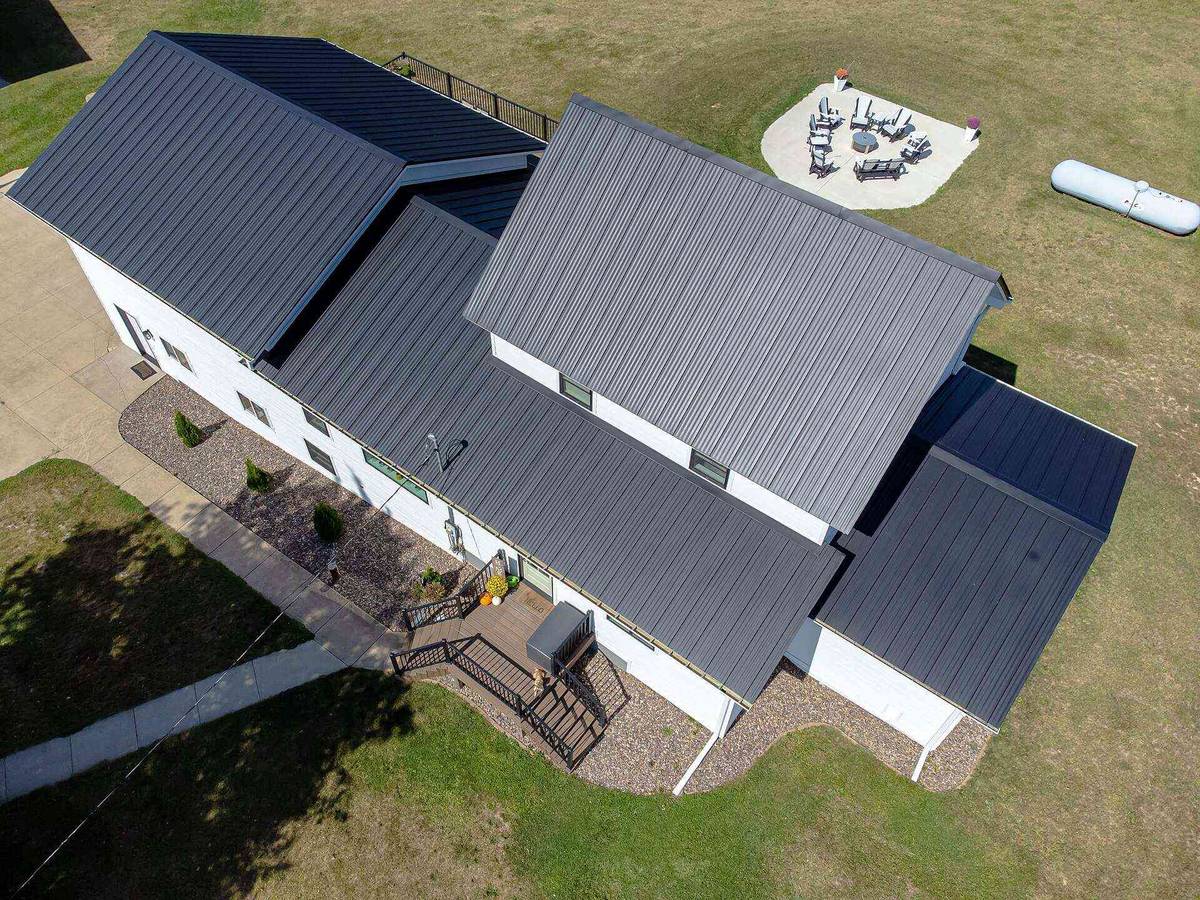 Aerial view of a white farmhouse with a black standing-seam metal roof